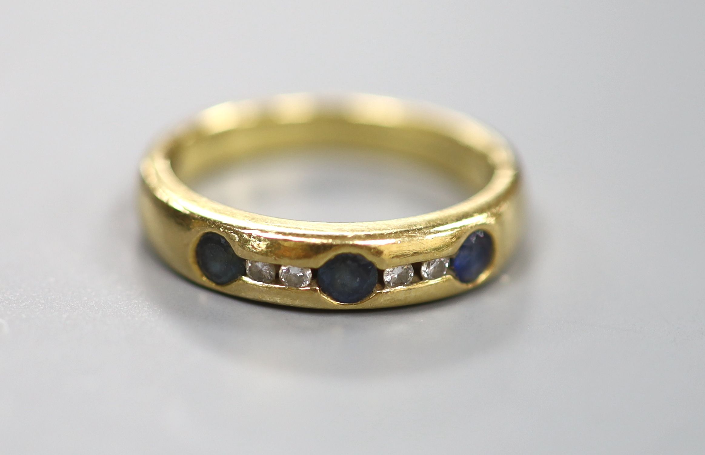 A modern 750 yellow metal, sapphire and diamond set half hoop ring, size N/O, gross 5.6 grams.